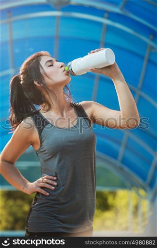 Fitness beautiful woman drinking water and sweating after exercising on summer hot day in city. Female athlete after work out.