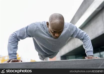 Fitness black man exercising push ups. Male model cross-training in urban background African guy in his twenties doing workout outdoors in the street.