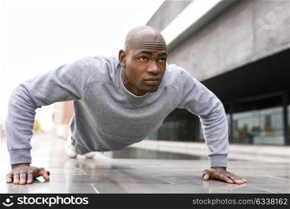 Fitness black man exercising push ups. Male model cross-training in urban background African guy in his twenties doing workout outdoors in the street.