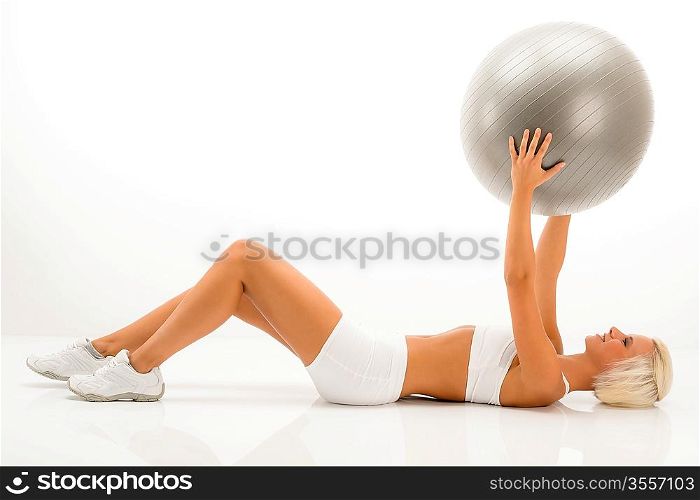 Fitness blonde woman exercising with Pilates ball lying white floor