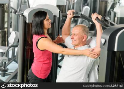 Fitness center personal trainer assist man exercise shoulder on machine