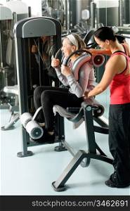 Fitness center senior woman exercise on machine with personal trainer