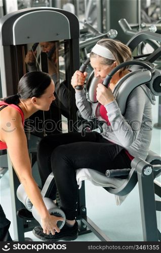Fitness center senior woman exercise with personal trainer on machine