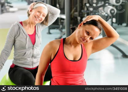 Fitness center senior woman with trainer stretching on swiss ball