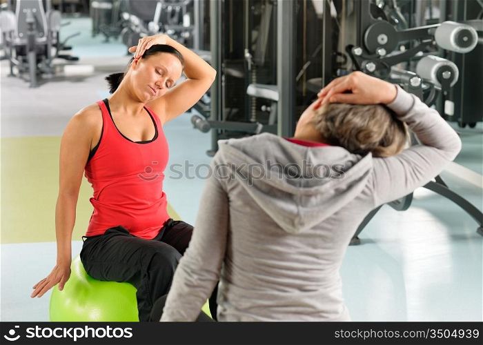 Fitness center senior woman with trainer stretching on swiss ball