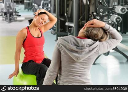 Fitness center senior woman with trainer stretching on swiss ball
