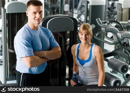 Fitness center young woman posing with personal trainer by gym machine