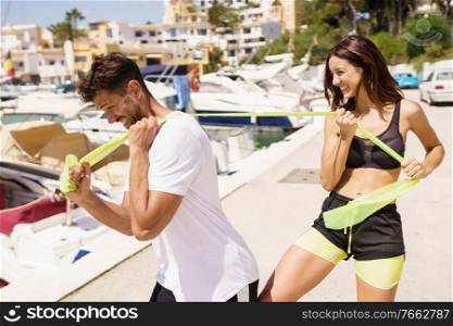Fitness couple in sportswear outfit working out with a elastic band on waterfront harbour.. Couple in sportswear outfit working out with a elastic band on waterfront harbour.
