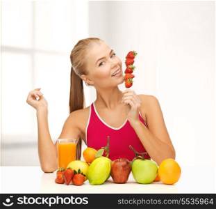 fitness, diet and food concept - young woman with organic food or fruits eating strawberry