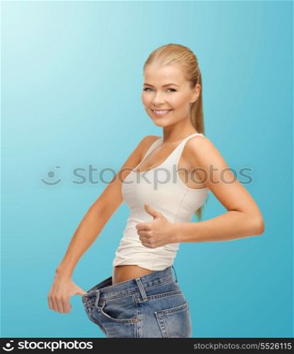 fitness, diet and good shape concept - sporty woman showing big pants and thumbs up