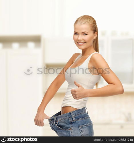 fitness, diet and good shape concept - sporty woman showing big pants and thumbs up