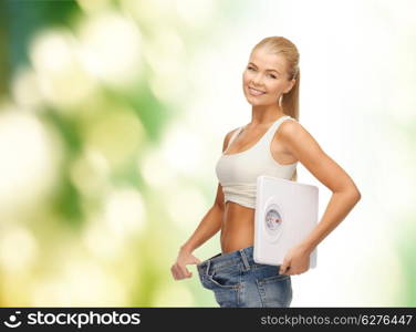 fitness, diet and healthcare concept - sporty woman showing big pants and holding scales