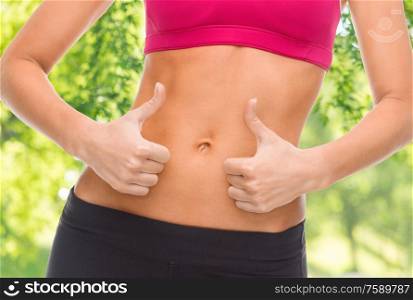 fitness, diet and people concept - close up of female abdomen and hands showing thumbs up over green natural background. close up of woman showing tummy and thumbs up