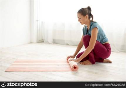 fitness equipment, sport and healthy lifestyle concept - woman rolling up mat at yoga studio or gym. woman rolling up mat at yoga studio or gym