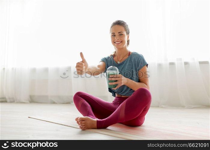 fitness equipment, sport and healthy lifestyle concept - young woman with cup of green smoothie at yoga studio or gym. woman with cup of smoothie at yoga studio