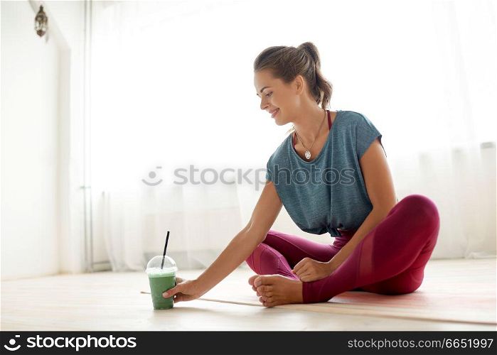 fitness equipment, sport and healthy lifestyle concept - young woman with cup of smoothie at yoga studio or gym. woman with cup of smoothie at yoga studio