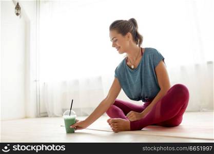 fitness equipment, sport and healthy lifestyle concept - young woman with cup of smoothie at yoga studio or gym. woman with cup of smoothie at yoga studio