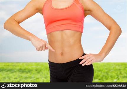 fitness, exercise and diet concept - close up of woman pointing finger at her six pack