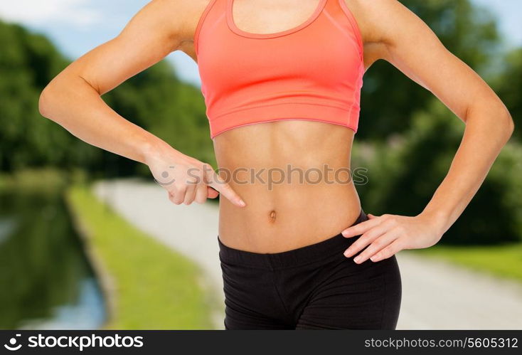 fitness, exercise and diet concept - close up of woman pointing finger at her six pack