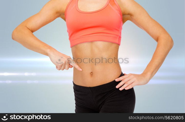 fitness, exercise and diet concept - close up of woman pointing finger at her six pack