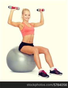fitness, exercise and diet concept - smiling sporty woman with dumbbells sitting on fitness ball