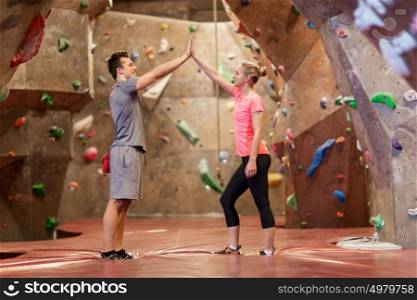 fitness, extreme sport, bouldering, people and healthy lifestyle concept - man and woman exercising at indoor climbing gym and making high five gesture. man and woman exercising at indoor climbing gym