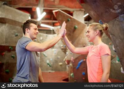 fitness, extreme sport, bouldering, people and healthy lifestyle concept - man and woman exercising at indoor climbing gym wall and making high five gesture. happy man and woman at indoor climbing gym wall