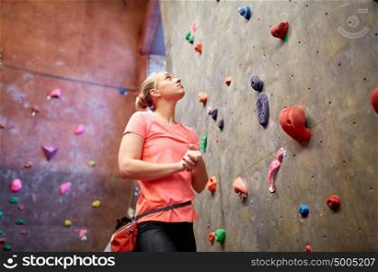 fitness, extreme sport, bouldering, people and healthy lifestyle concept - young woman with chalk bag exercising at indoor climbing gym wall. young woman exercising at indoor climbing gym wall