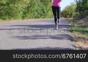 Fitness female runner jogging along road at summer