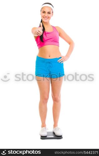 Fitness female standing on weight scale and showing thumbs up