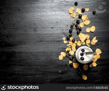 Fitness food. Milk dessert with wheat flakes and wild black currants. On a black wooden background.. Milk dessert with wheat flakes and wild black currants.