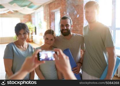 fitness, friendship and healthy lifestyle concept - group of happy people at yoga studio or gym taking picture on smartphone. happy people at yoga studio or gym photographing. happy people at yoga studio or gym photographing