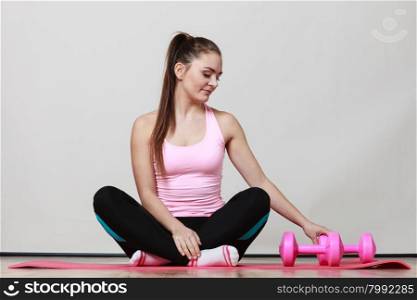 Fitness girl fit woman sitting on exercise mat with dumbbells, doing exercise with dumb bells training gray background