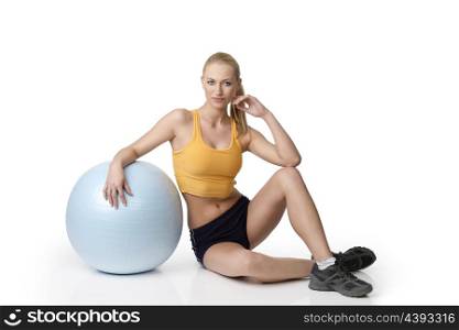 fitness girl in gym dress sitting on white with a ball near her . natural skin