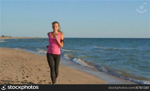 Fitness girl jogging on beach listening music in wireless headset during workout