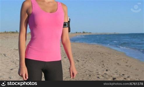 Fitness girl with phone in arm sport band exercising on the beach