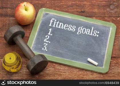 fitness goals list - slate blackboard sign against weathered red painted barn wood with a dumbbell, apple and tape measure