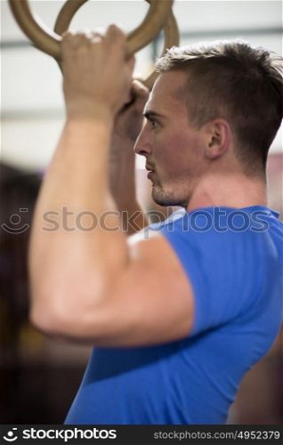 Fitness handsome man doing dipping exercise using rings in the gym