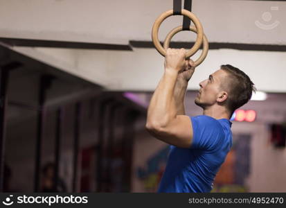 Fitness handsome man doing dipping exercise using rings in the gym