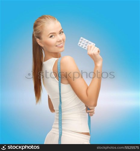 fitness, health, pharmacy and diet concept - sporty woman with measuring tape and diet pills