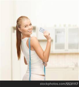 fitness, health, pharmacy and diet concept - sporty woman with measuring tape and diet pills
