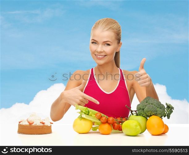 fitness, healthcare and diet concept - smiling woman with fruits and cake pointing at healthy food