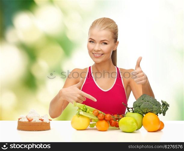 fitness, healthcare and diet concept - smiling woman with fruits and cake pointing at healthy food