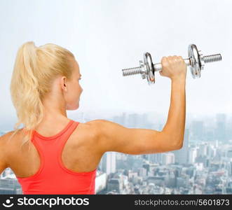 fitness, healthcare and exercise concept - young sporty woman with heavy steel dumbbell from the back