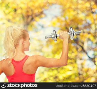 fitness, healthcare and exercise concept - young sporty woman with heavy steel dumbbell from the back