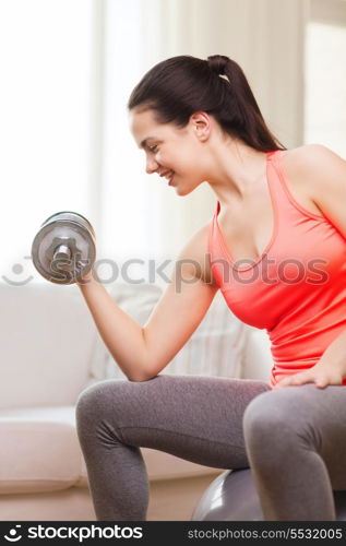 fitness, home and diet concept - smiling girl exercising with fitness ball and dumbbells at home