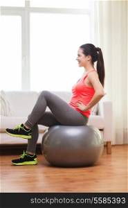 fitness, home and diet concept - smiling girl exercising with fitness ball at home