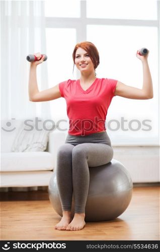 fitness, home and diet concept - smiling redhead girl exercising with fitness ball and dumbbells at home