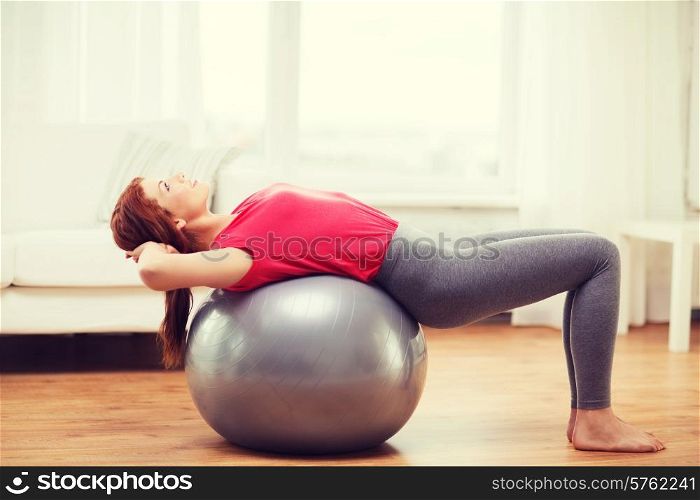 fitness, home and diet concept - smiling redhead girl exercising with fitness ball at home