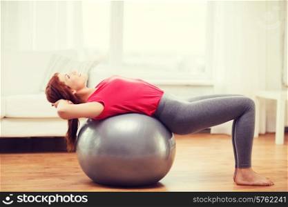 fitness, home and diet concept - smiling redhead girl exercising with fitness ball at home